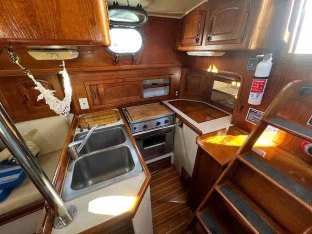 Slide: The Image of 1986 Pacific Seacraft 37 sailboat galley with wooden cabinetry, stove, sink, and stairs. - 12