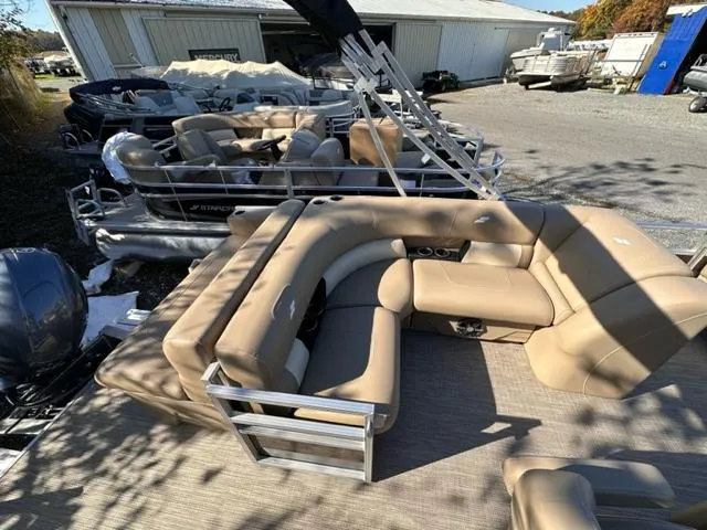 Slide: The Image of 2024 Starcraft LX 20 CB pontoon boat with tan seating, docked at a marina. - 2