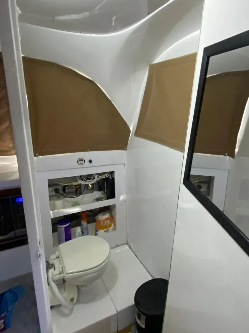 Slide: The Image of 1973 Bertram 31 boat bathroom with toilet, storage shelves, and mirror. - 6