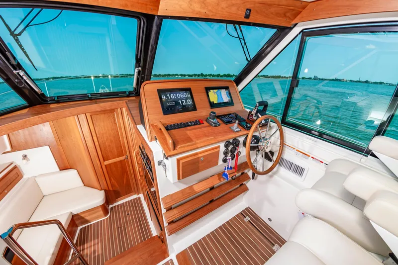 Slide: The Image of 2025 Back Cove 39O boat interior with wooden helm, navigation screens, and ocean view. - 20