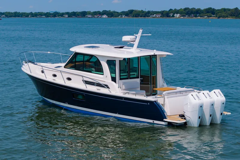 Slide: The Image of 2025 Back Cove 39O boat on calm water, featuring sleek design and triple outboard engines. - 7