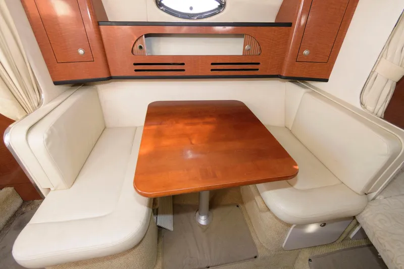 Slide: The Image of 2005 Sea Ray 280 Sundancer cabin dinette with wooden table and cushioned seating. - 8