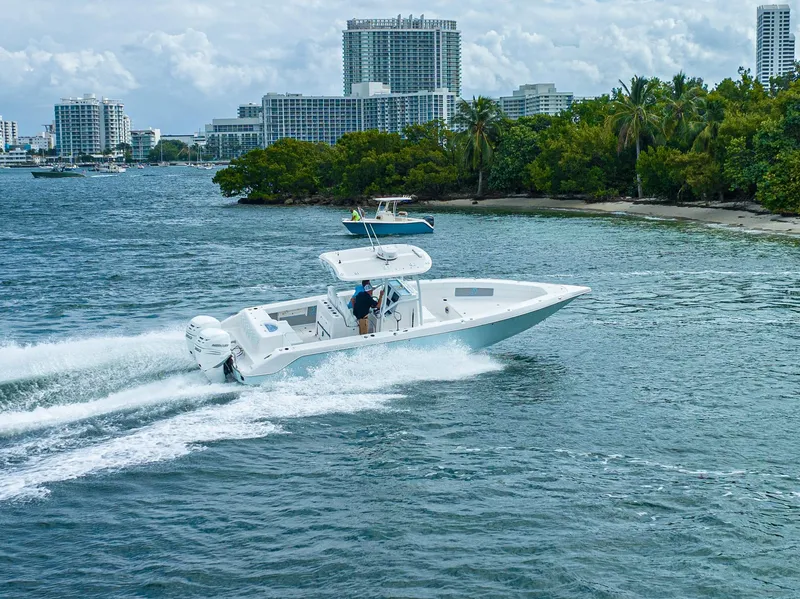 Slide: The Image of 2023 CG Boat Works 35 M-Series cruising near a tropical shoreline with cityscape in the background. - 7