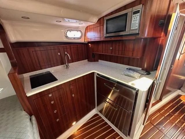 Slide: The Image of 2012 Pursuit OS 375 Offshore boat kitchen with wood cabinetry, microwave, sink, and refrigerator. - 15