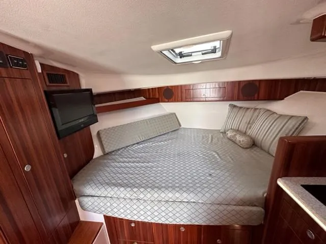 Slide: The Image of 2012 Pursuit OS 375 Offshore cabin with bed, TV, and wooden cabinetry. - 16