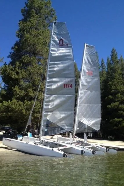 Slide: The Image of 1989 Nacra 5.8 catamaran with sails, docked by a forested lakeside. - 21