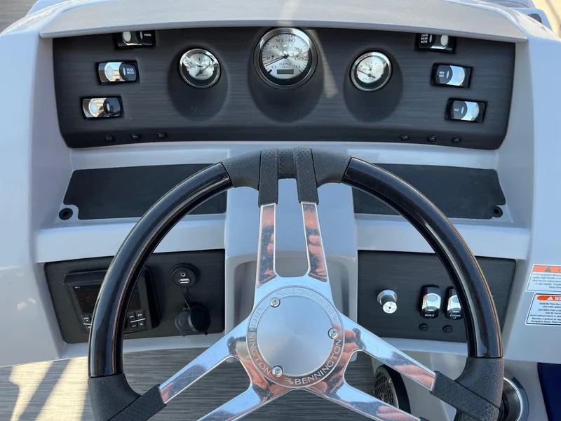 Slide: The Image of Steering wheel and dashboard of 2023 Bennington 25LSRTDSP boat, featuring gauges and controls. - 20