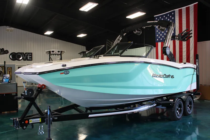 The Image of 2024 MasterCraft NXT22 boat on trailer in showroom with American flag. - 0
