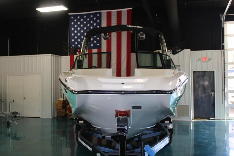 Slide: The Image of 2024 MasterCraft NXT22 boat in showroom with American flag backdrop. - 2