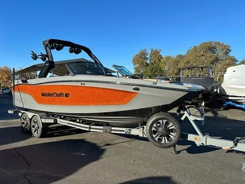 Slide: The Image of 2024 MasterCraft XT24 boat on trailer, orange and gray, parked outdoors. - 4
