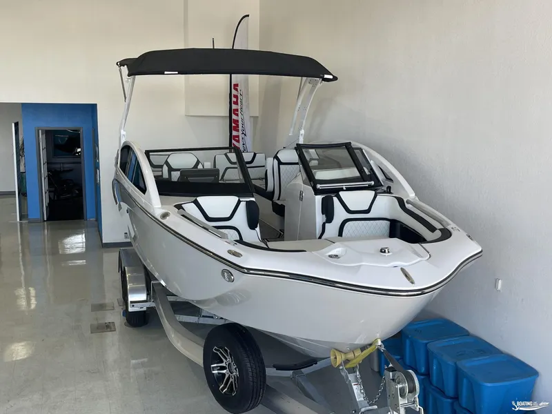 Slide: The Image of 2024 Yamaha Boats 275 SE in showroom, sleek design, white exterior, black accents. - 2