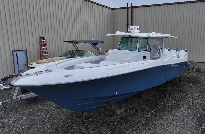 Slide: The Image of 2025 HCB 42 Lujo boat with blue hull, docked outdoors near a warehouse. - 0