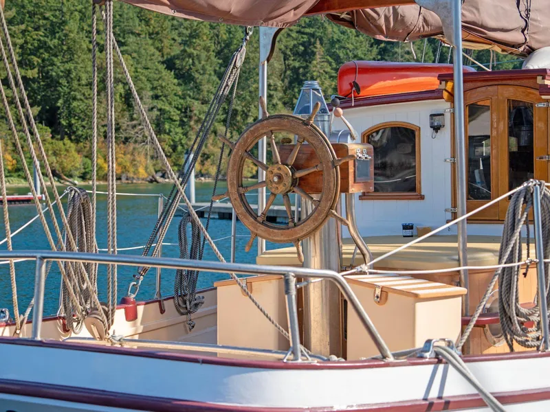 Slide: The Image of Sailboat deck with wooden wheel, Custom Prothero & Franken, 1997, docked by forested shoreline. - 12