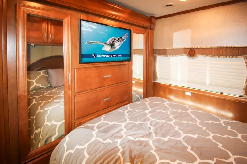 Slide: The Image of 2012 Thor 37DT RV bedroom with TV, wooden cabinets, and patterned bedding. - 18