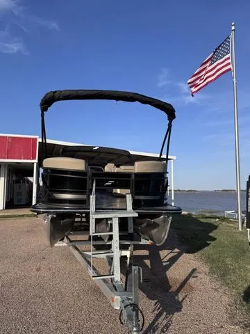 Slide: The Image of 2023 Starcraft CX23FD boat on trailer near lake and American flag. - 2