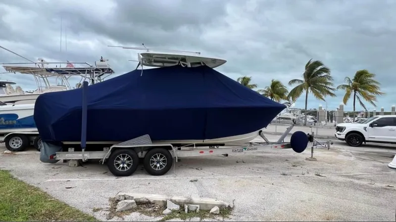 Slide: The Image of 2018 Sea Hunt 235 boat on trailer with blue cover, parked near palm trees. - 16