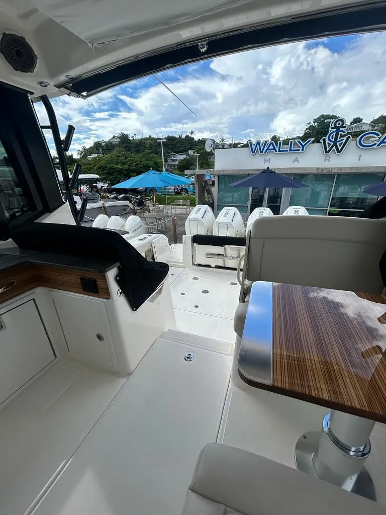 Slide: The Image of 2024 Boston Whaler 405 Conquest interior with seating and table, marina view in background. - 5