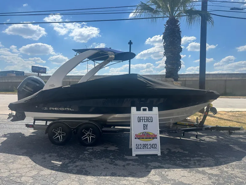 The Image of 2023 Regal 21 OBX boat on trailer, covered, with sale sign in sunny outdoor setting. - 0