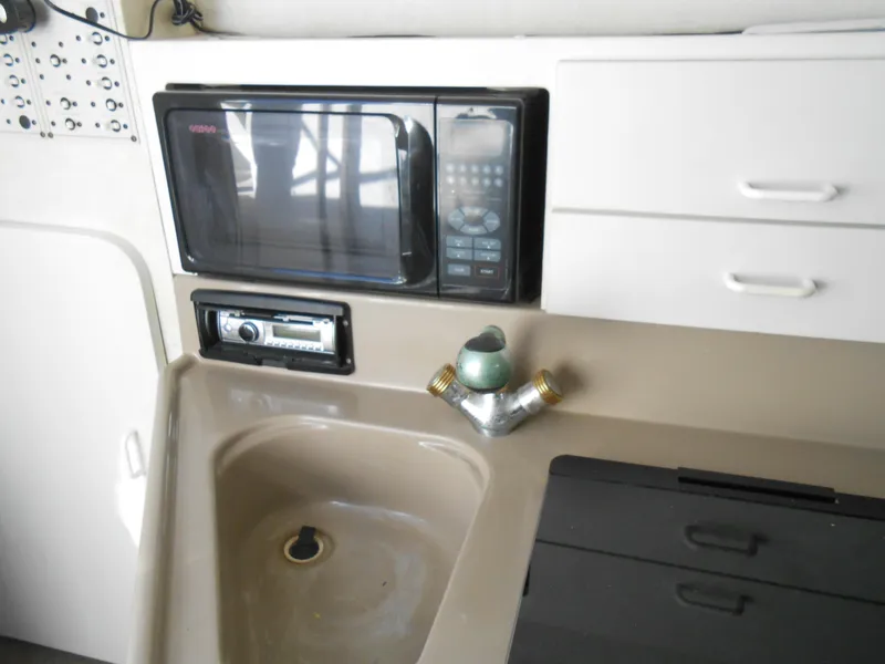Slide: The Image of 2003 Glastron GS249 boat kitchenette with microwave, sink, and storage cabinets. - 28