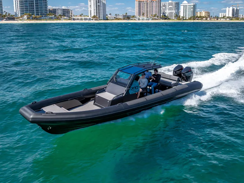 Slide: The Image of 2024 Goldfish X10 Scout boat cruising on clear blue water near a coastal city. - 2