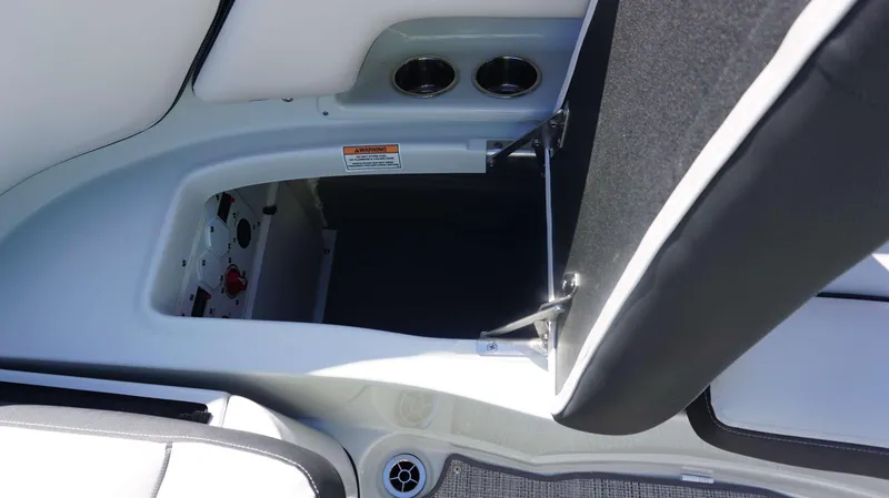 Slide: The Image of Open storage compartment in 2024 Crownline 290 XSS boat with cup holders and warning label. - 14