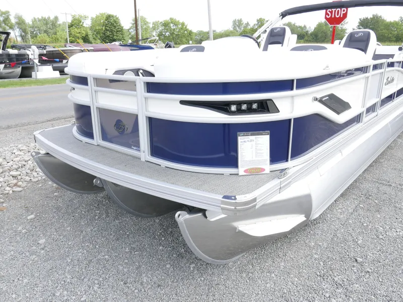 Slide: The Image of 2024 Barletta Corsa 23UC pontoon boat, blue and white, parked on gravel. - 2