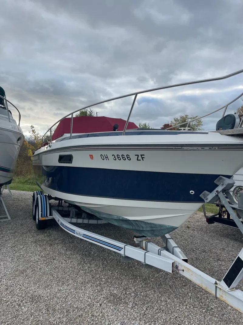 The Image of 1988 Regal boat on trailer, blue and white, parked outdoors under cloudy sky. - 0