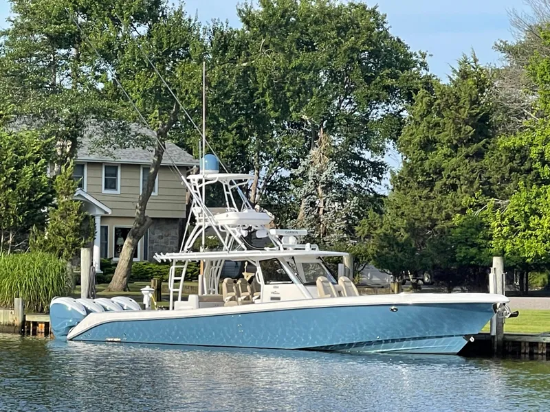 The Image of 2019 Everglades 435 CC boat docked by a waterfront home, surrounded by lush greenery. - 0
