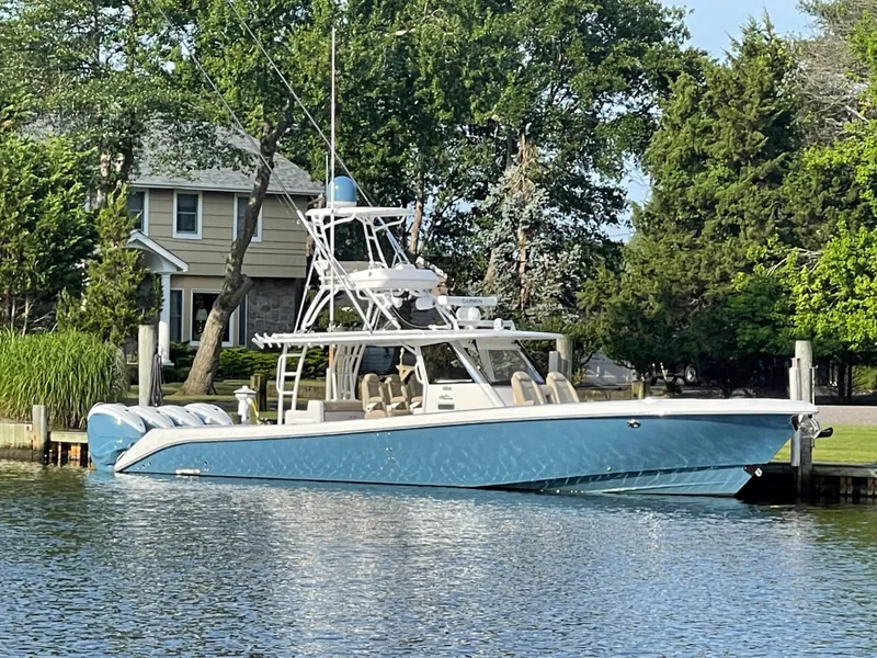 Slide: The Image of 2019 Everglades 435 CC boat docked by a waterfront home, surrounded by lush greenery. - 1