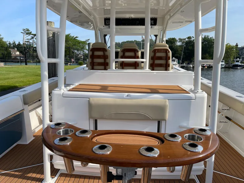 Slide: The Image of 2019 Everglades 435 CC boat interior with seating and rod holders, docked by a scenic waterfront. - 13