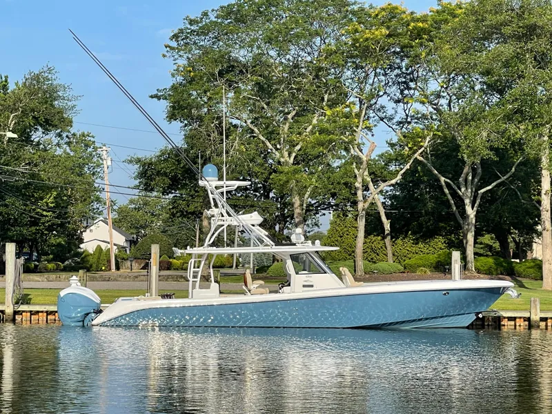 Slide: The Image of 2019 Everglades 435 CC boat docked on a calm lake with trees in the background. - 2
