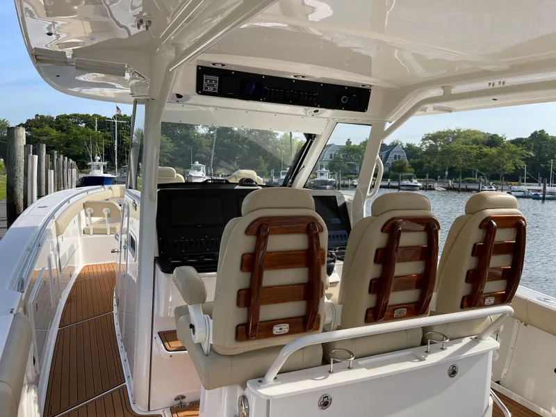 Slide: The Image of 2019 Everglades 435 CC boat interior with helm seats and wooden deck, docked by the water. - 26