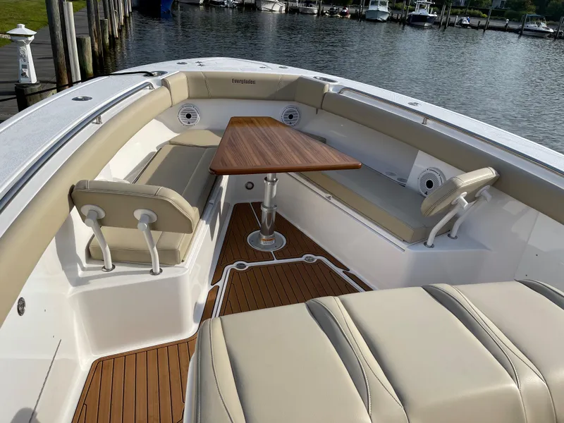 Slide: The Image of 2019 Everglades 435 CC boat interior with seating and wooden table by the water. - 43