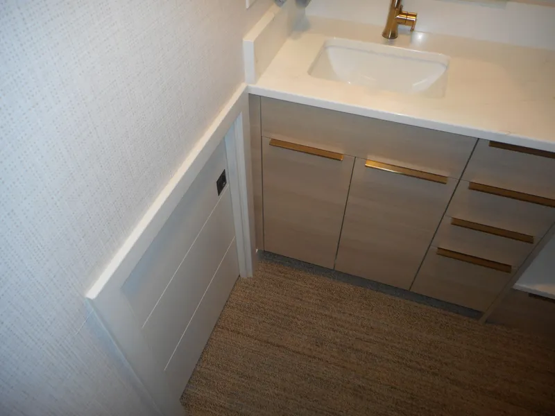 Slide: The Image of Modern bathroom vanity with gold accents, beige cabinetry, and textured flooring. Adonia Radiance Share #12, 2022. - 31