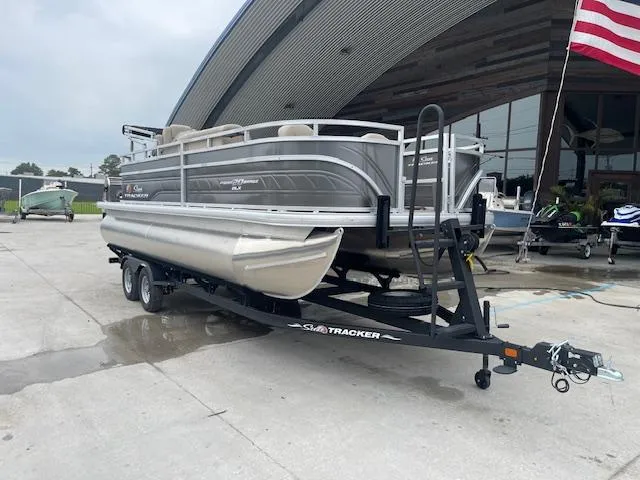 Slide: The Image of 2024 Sun Tracker Fishin' Barge 20 DLX pontoon boat on trailer outside a boat dealership. - 2