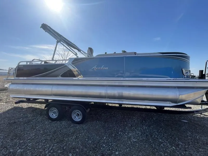 The Image of 2024 Avalon LSZ Versatile Rear Lounger pontoon boat on a trailer under a bright sky. - 1
