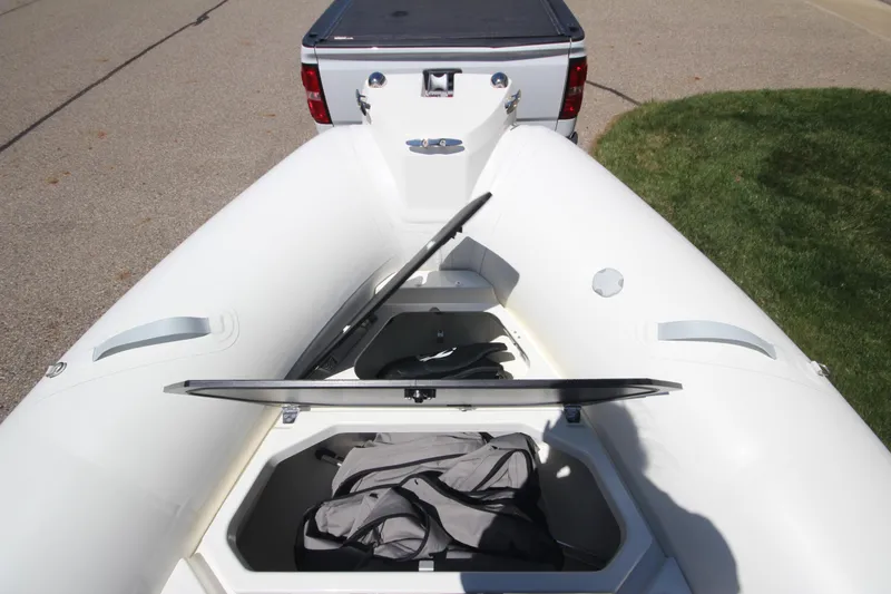 Slide: The Image of 2025 Zodiac Medline 5.8 NEO boat with open storage compartment, parked near a truck. - 9