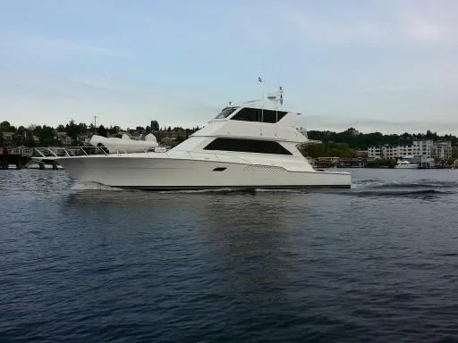 Slide: The Image of 2000 Viking 72 Convertible yacht cruising on calm waters near a coastal town. - 2