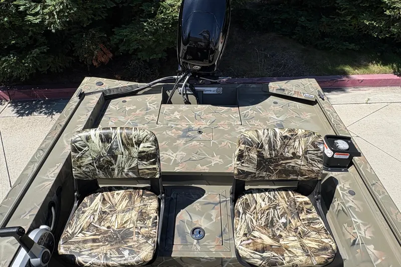 Slide: The Image of 2024 Tracker Grizzly 1754 SC boat with camouflage seats and motor, parked outdoors. - 14