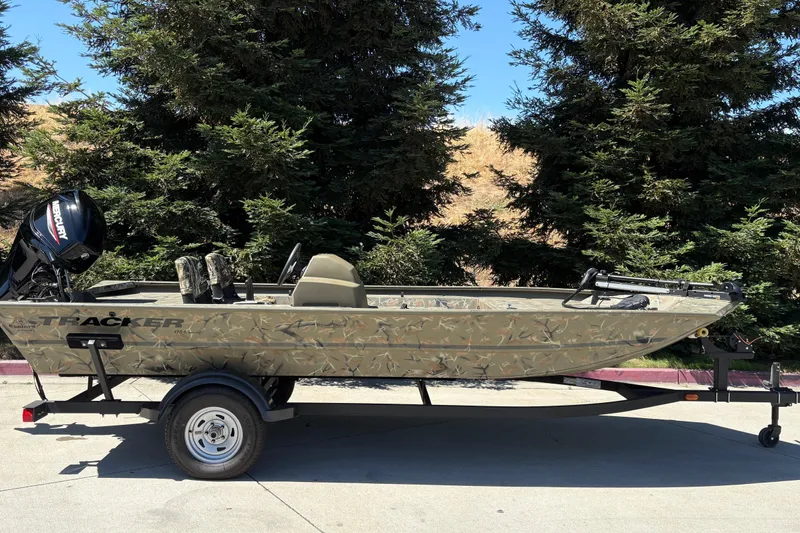 The Image of 2024 Tracker Grizzly 1754 SC boat on trailer, camo design, parked outdoors. - 0