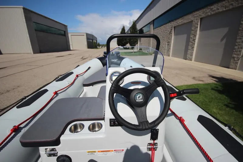 Slide: The Image of 2024 Zodiac Open 4.8 NEO 70hp boat, steering console view, docked near industrial buildings. - 13