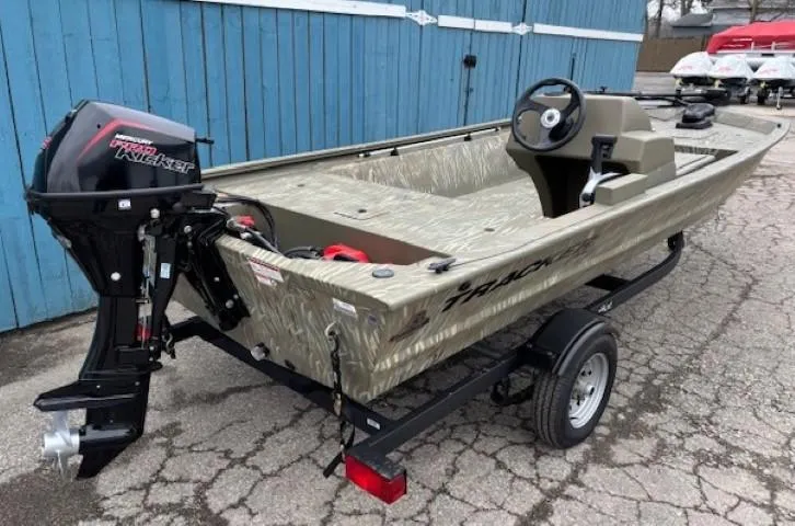 Slide: The Image of 2024 Tracker Grizzly 1648 SC boat on trailer, parked near blue building. - 2