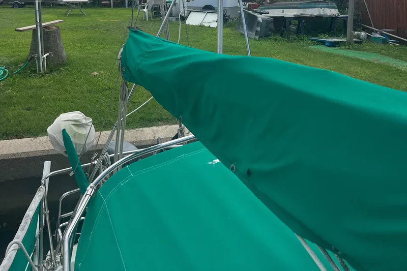 Slide: The Image of 1974 CAL T2 sailboat with green cover docked near grassy area. - 6