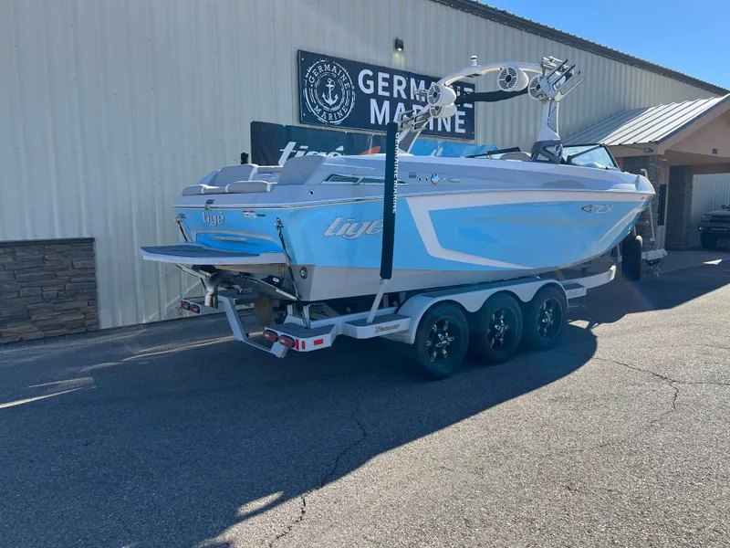 Slide: The Image of 2021 Tigé 25ZX boat on a trailer outside a marine dealership. - 1