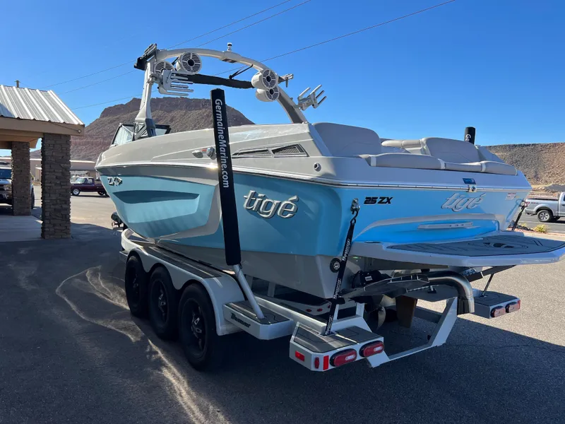 Slide: The Image of 2021 Tigé 25ZX boat on a trailer, blue and white, parked outdoors. - 2