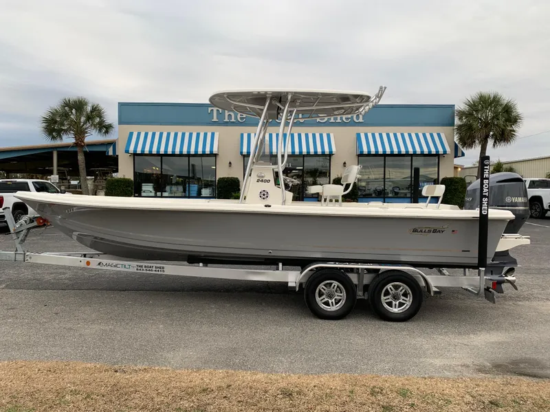 The Image of 2025 Bulls Bay 2400 boat on trailer, parked outside a store with blue-striped awnings. - 1
