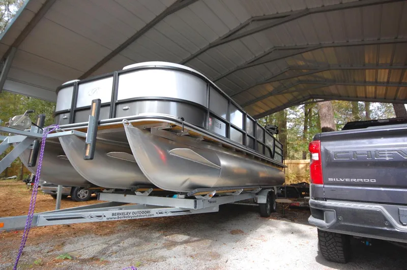 Slide: The Image of 2021 Bentley Pontoons 243 Swingback on trailer under a carport, next to a Chevrolet Silverado. - 2