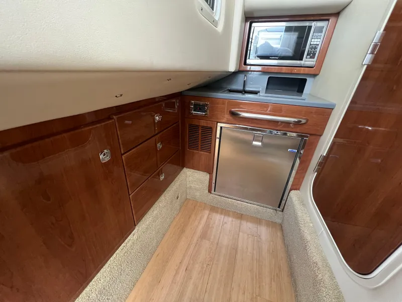 Slide: The Image of 2014 Formula 350 Crossover Bowrider interior kitchen with microwave, fridge, and wooden cabinets. - 44