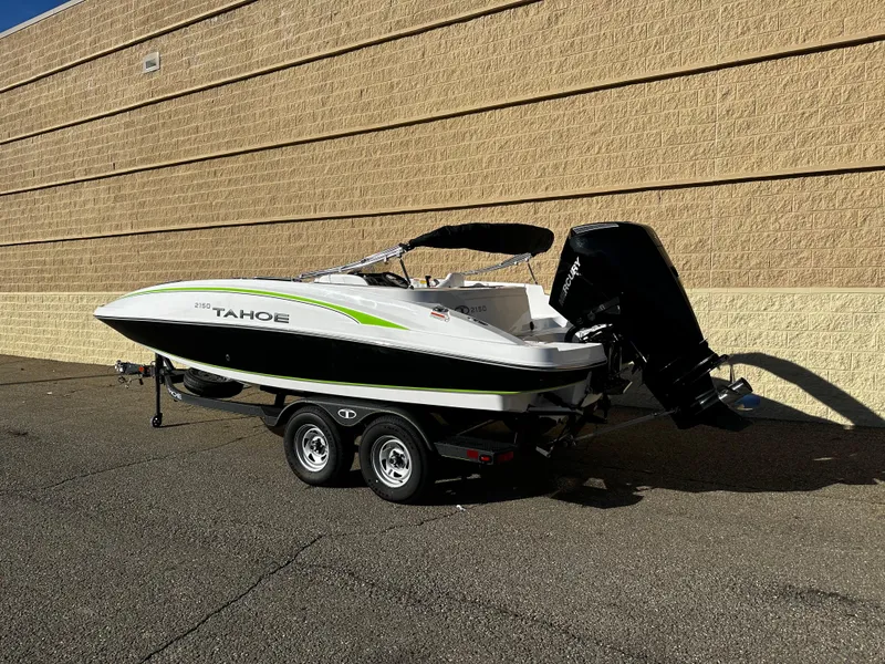 Slide: The Image of 2024 Tahoe 2150 boat on trailer, parked beside a beige wall. - 2