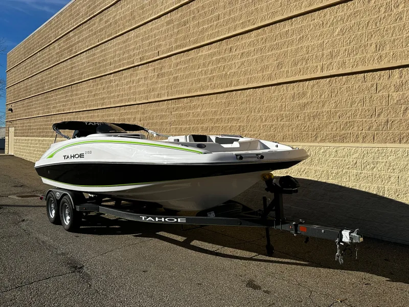 Slide: The Image of 2024 Tahoe 2150 boat on trailer, parked beside a beige brick wall. - 7